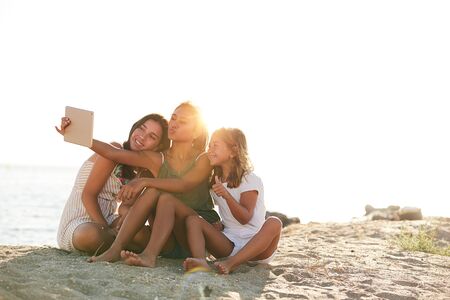 Three girls on the beach taking a picture with a tabletの写真素材