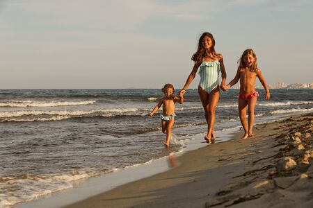 three girls running on the beach holding handsの写真素材