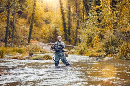 Senior person fishing for trout and salmon in a riverの写真素材