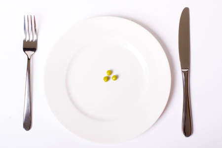Green peas on white plate with knife and fork, with soft shadowの写真素材