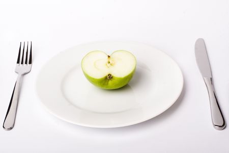 Green apple on white plate with knife and fork, with soft shadowの写真素材