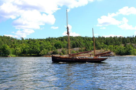 two-masted sailing ship in the background of the forest, rocks and blue sky