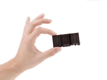 Hand holds tasty morsel of dark chocolate. White background.の写真素材
