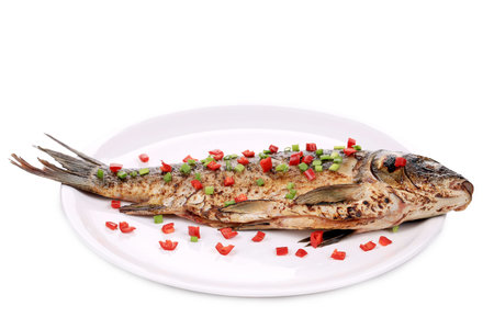 Fried fish on a white plate with pieces of green onion and red chili pepper