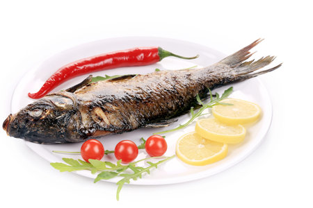 Fried fish on white plate with lemon slices, tomato and chili pepper