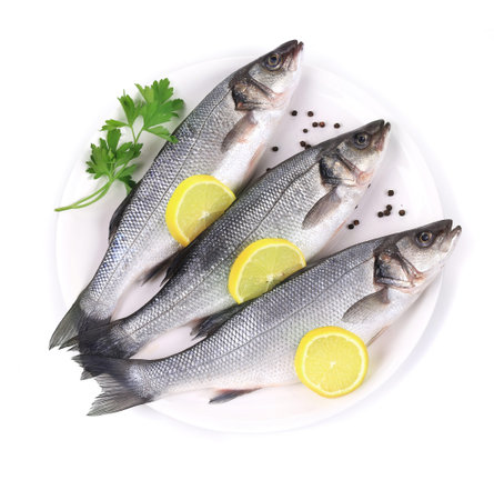 Three fresh seabass with lemon on plate. Isolated on a white background.