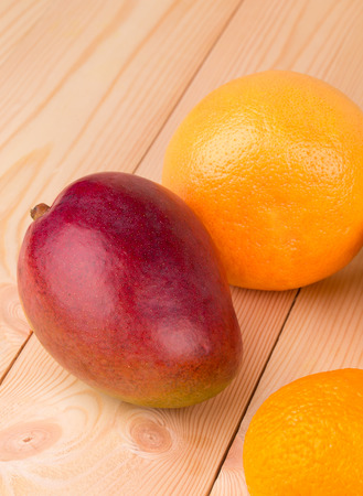 Colorful festive assortment of mango and citrus fruits arranged on a wooden boardの写真素材