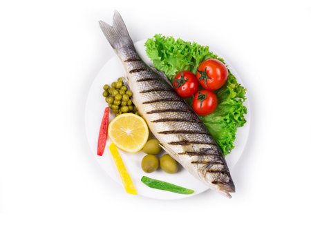 Grilled seabass with vegetables on plate. Isolated on a white background.