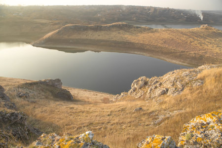 A panoramic view of beautiful river banks with grassy rocks and sky reflected in still waters