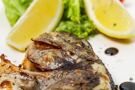 Grilled sea bass closeup with lemon and herbs. As a whole background..