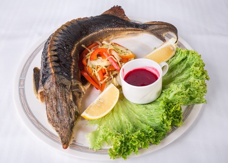 Baked sturgeon with vegetables and sweet red sauce. Plate located on a white canvas tablecloth background.の写真素材