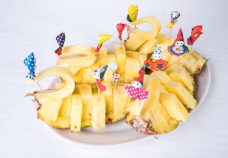Delicious sliced pineapple with paper umbrellas. Plate located on a white canvas tablecloth background.の写真素材