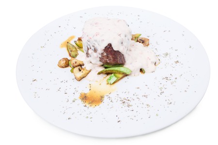 Grilled beef steak covered with delicious sauce and zucchini with champignons as a garnish. Isolated on a white background.の写真素材