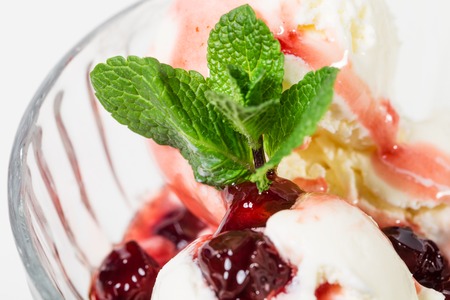 Glass cup full of delicious vanilla ice cream with cherry jam and fresh mint. Isolated on a white background.の写真素材