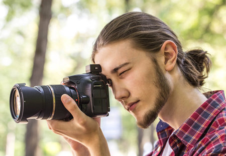 Male photographer taking photos with DSLR digital camera at outdoors. Side view.