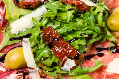 Italian salami and prosciutto platter with grated parmesan and fresh arugula covered with balsamic vinegar. Macro. Photo can be used as a whole background.の写真素材