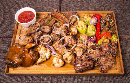 Mixed various grilled meat platter with vegetables and spicy tomato sauce. Located on a brown canvas...