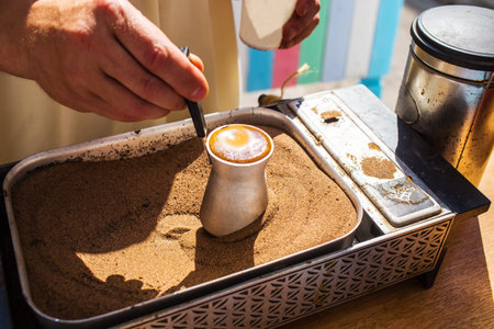 Hand holding coffee turk on sand. Turkish coffee prepared on a hot yellow sand for an beautiful...