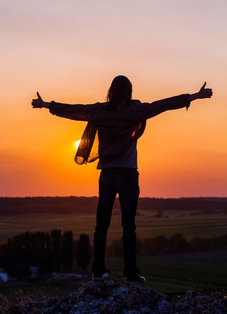 Silhouette of young longhair male model with thumbs-up hands at red and purple sunset sky.の写真素材
