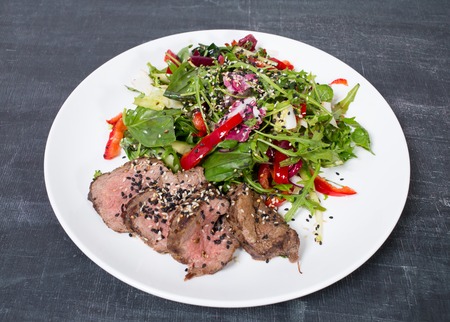 Grilled thai beef salad with fresh herbs. Plate located on a black table as a background.の写真素材