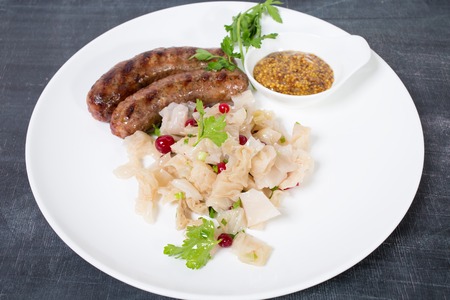 Grilled sausages with sauerkraut and mustard. Plate located on a black table as a background.の写真素材