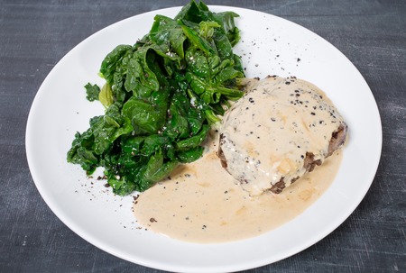 Grilled pork fillet with mushroom sauce and delicious spinach. Plate located on a black table as a background.の写真素材