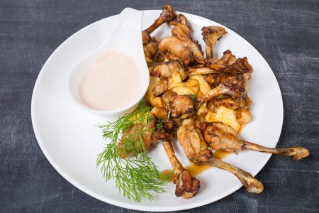 Chicken legs with melted cheese and delicious sauce. Plate located on a black table as a background.の写真素材