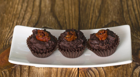 Set of chocolate candies with a fondant and dried tomato. Close up on the wooden background.