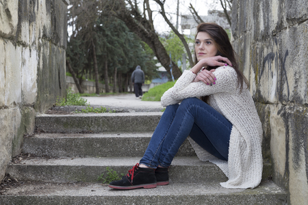 Quarrel and parting. Sad lonely girl sitting on the steps and her boyfriend go away into the distance.の写真素材