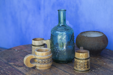 Moldavian still life. The blue lime wall. There are traditional wooden mugs and a blue glass bottle.の写真素材