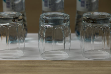 Three inverted empty glasses on a wooden surface. Blurry plastic bottles in the background. Close-up.の写真素材
