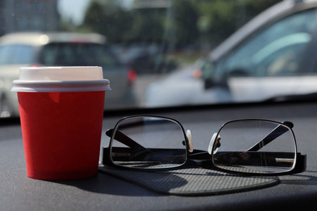 Glasses for vision correction and cup of coffee are on the car dashboard. Close-up. The background is blurred.の写真素材