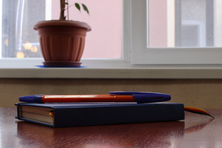 Workplace near a window with a notebook and a pen. Copy space. Modern a desk near window at office. Morning time with warm light. Business concept.の写真素材