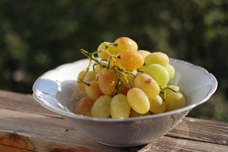 A bunch of amber grapes in a white bowl. Green blurred background. Close-up.の写真素材