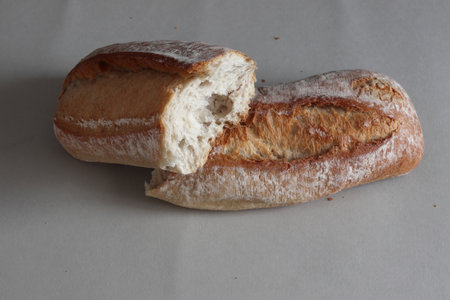 A broken freshly baked rustic baguette. It is located on a gray background. Close-up.の写真素材