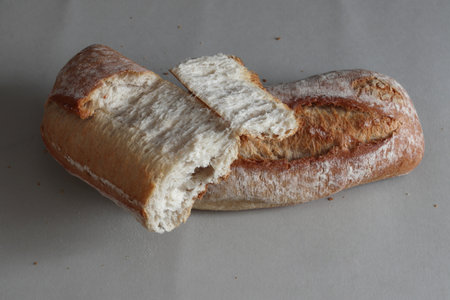 A broken freshly baked rustic baguette. It is located on a gray background. Close-up.の写真素材
