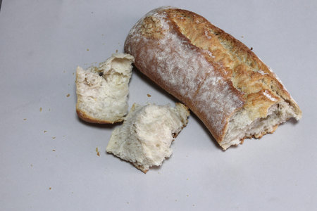 A broken freshly baked rustic baguette. It is located on a gray background. Close-up.