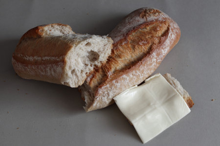 A broken freshly baked rustic baguette with cheese. It is located on a gray background. Close-up.