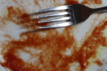 Empty dirty white plate with tomato sauce or ketchup on it. A fork on white background. Close-up.の写真素材
