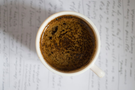 A cup of coffee on a piece of paper. Paper covered with inscriptions. Close-up.