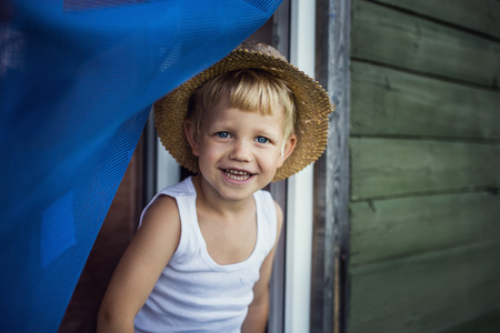 Cheerful kid with straw hat leaning out a window  の写真素材