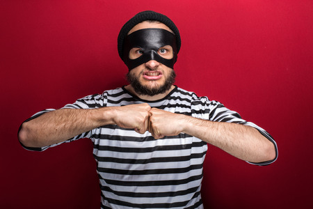 Portrait of a angry bandit threaten with fist on red backgroundの写真素材