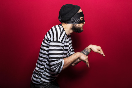 A thief with mask slinking on red background  の写真素材