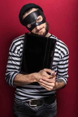 Thief stealing a laptop computer  Portrait on red background  の写真素材