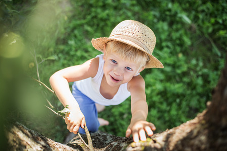 Outdoor portrait: beautiful child with a straw hat climbs in a treeの写真素材