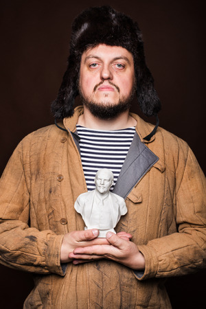 Serious russian man holding Lenin sculpture. Studio portrait isolated on brown backgroundの写真素材
