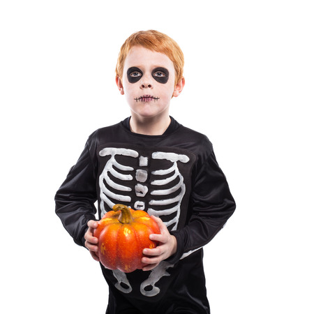 Portrait of little red haired boy wearing halloween skeleton costume and holding pumpkin isolated over white backgroundの写真素材