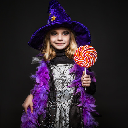 Little beautiful halloween witch with colorful candy. Studio portrait over black backgroundの写真素材