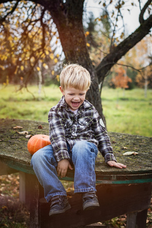 Beautiful casual blond child sitting outdoor on table and laughing. Autumn. Outdoor portraitの写真素材
