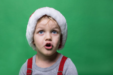 Surprised child with red Santa Claus cap looking up. Big blue eyes. Christmas concept. Studio...